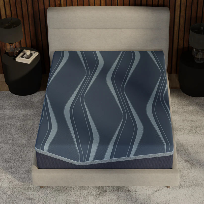 Blue patterned mattress cover on a bed in a room with a lamp and nightstand.