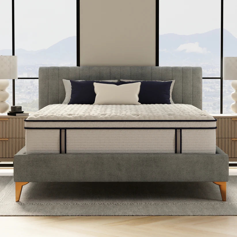 Gray upholstered bed with white mattress in a room with large windows.