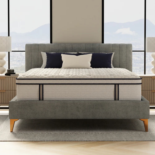 Gray upholstered bed with white mattress in a room with large windows.