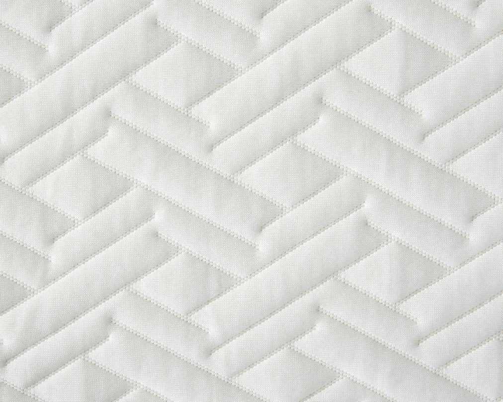 A close-up of a white quilted fabric with a geometric, zigzag pattern stitched into padded rectangular sections.