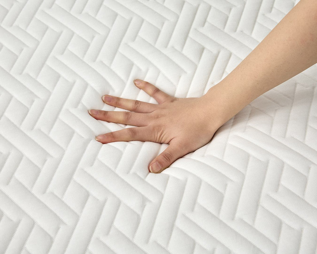 A close-up of a white quilted mattress topper or mattress surface with a hand pressing down to show its soft, responsive texture.
