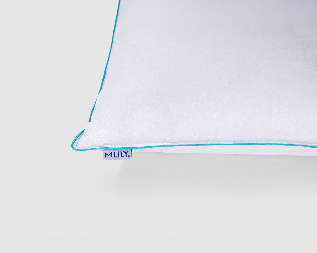 A close-up of a white pillow corner with a thin light blue piping edge and a small visible 'MILY' brand tag.