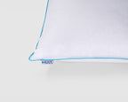 A close-up of a white pillow corner with a thin light blue piping edge and a small visible 'MILY' brand tag.
