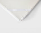 Close-up of a white mattress topper or mattress corner showing a textured white cover, a white mesh side panel, and a white elastic band on a plain white background.
