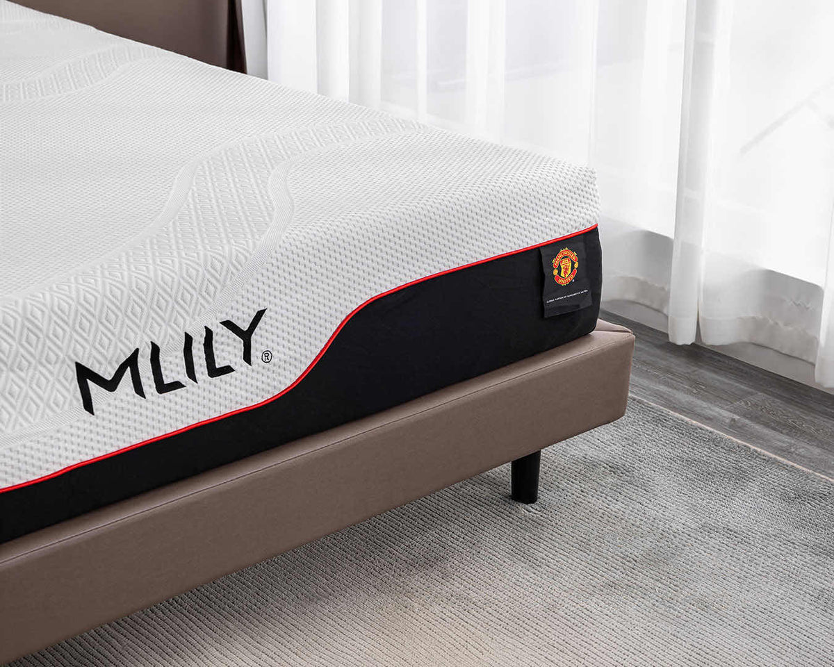A close-up of an MLILY mattress on a bed frame in a bedroom setting with white curtains and a gray rug.