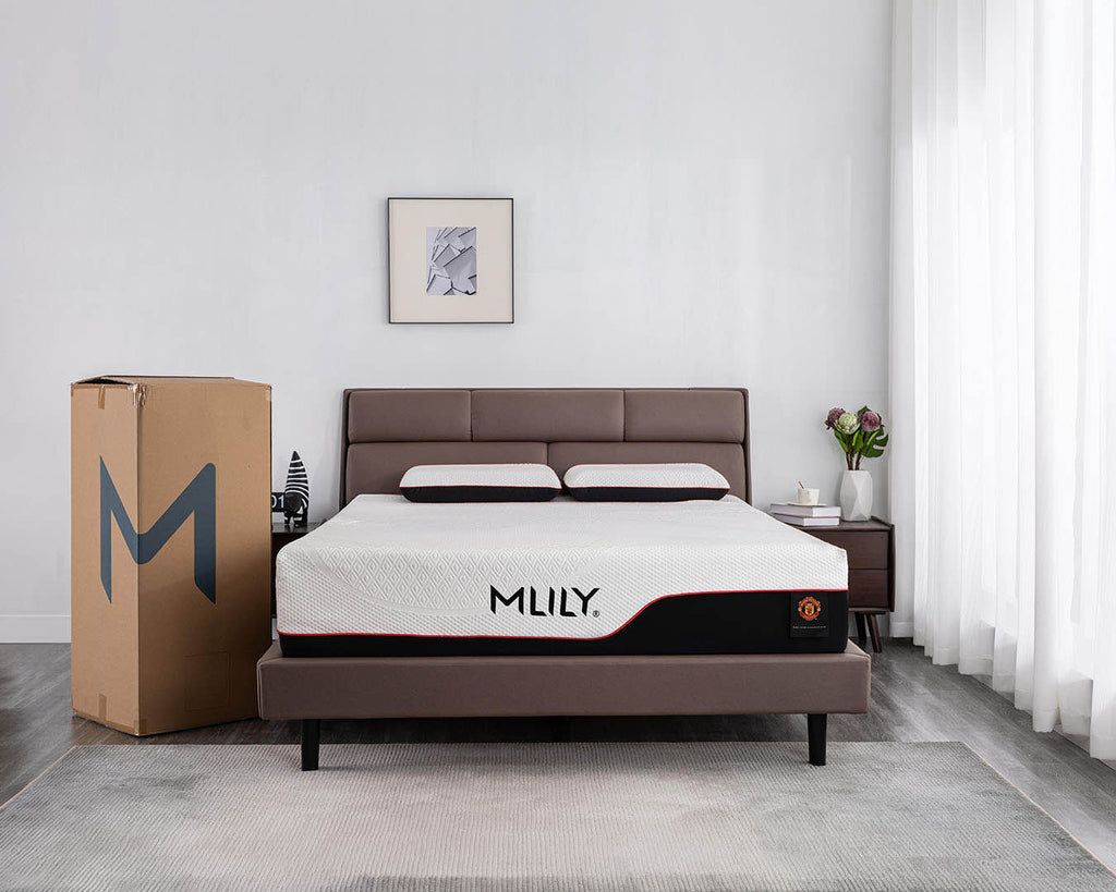 A bed with a brown upholstered frame and a white mattress featuring the brand name 'MLILY' on the side, shown in a modern bedroom setting next to a large branded cardboard box.
