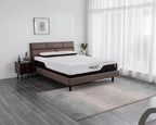A modern bedroom scene featuring a brown upholstered bed frame with a white mattress branded 'MULY' on the side, styled with a dark wood nightstand, gray rug, and sheer white curtains.